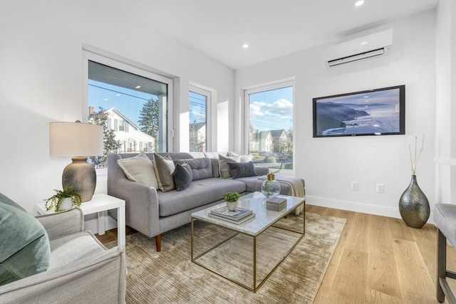 living area featuring a wall unit AC, light wood-style flooring, baseboards, and recessed lighting