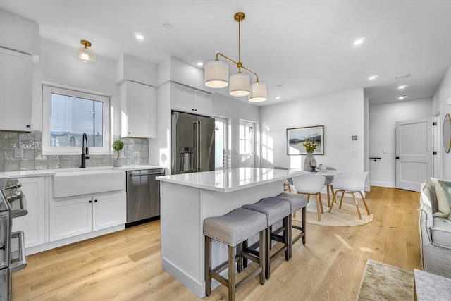 kitchen featuring white cabinets, stainless steel appliances, light countertops, pendant lighting, and a sink