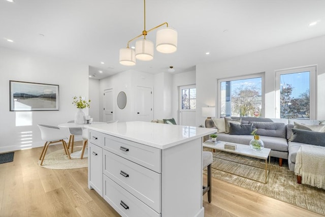 kitchen with open floor plan, decorative light fixtures, light countertops, light wood-style floors, and white cabinetry