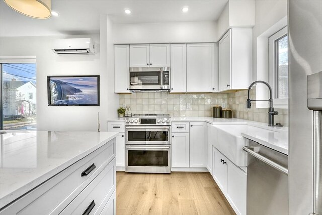 kitchen with stainless steel appliances, white cabinets, light stone counters, and a wall mounted AC