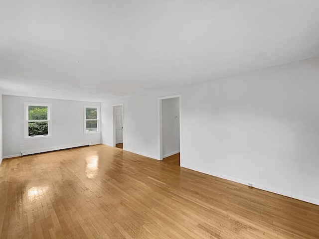 empty room featuring a baseboard heating unit, light wood finished floors, and baseboards