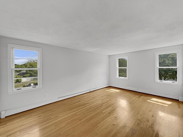 empty room with a wealth of natural light, baseboards, light wood finished floors, and baseboard heating