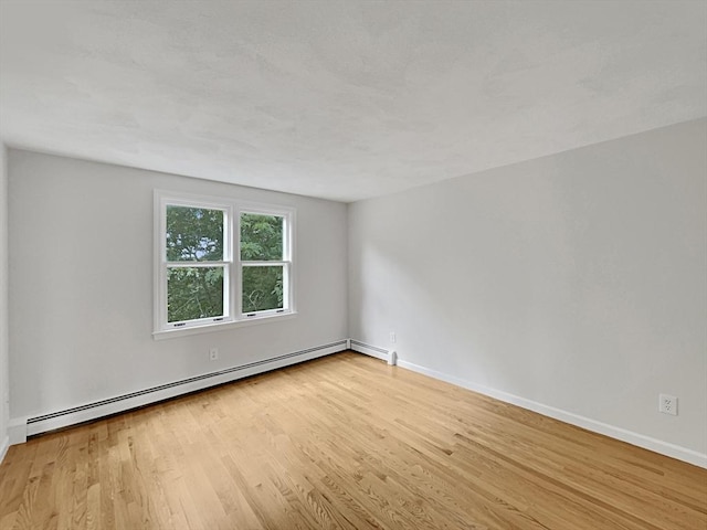 empty room with light wood-type flooring, a baseboard radiator, and baseboards