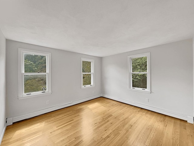 spare room featuring light wood-type flooring, a healthy amount of sunlight, and baseboard heating