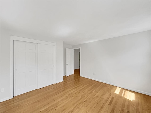 unfurnished bedroom featuring a closet, light wood-style flooring, and baseboards