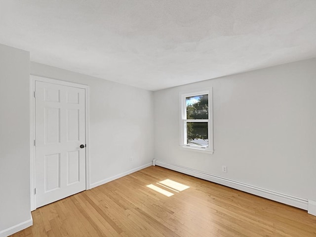 spare room with light wood finished floors, a baseboard radiator, and baseboards