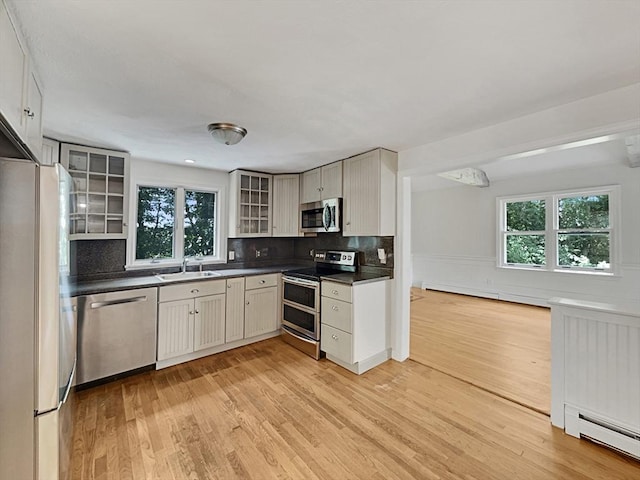 kitchen with a baseboard heating unit, stainless steel appliances, dark countertops, and glass insert cabinets