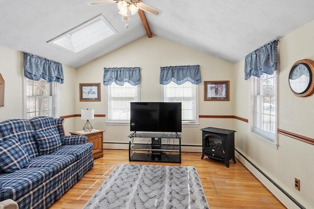 living room with vaulted ceiling with skylight, light wood-style flooring, baseboard heating, and a wood stove