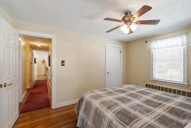 bedroom with radiator heating unit, wood finished floors, a ceiling fan, and baseboards