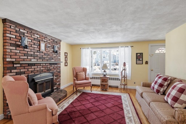 living area with a fireplace, radiator, a textured ceiling, wood finished floors, and baseboards