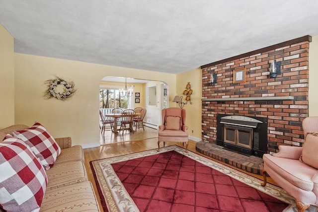 living area featuring arched walkways, a chandelier, wood finished floors, baseboards, and a brick fireplace