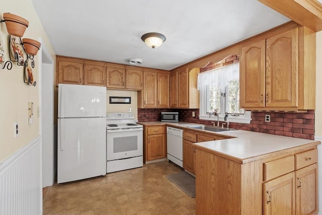 kitchen with a peninsula, white appliances, a sink, wainscoting, and light floors