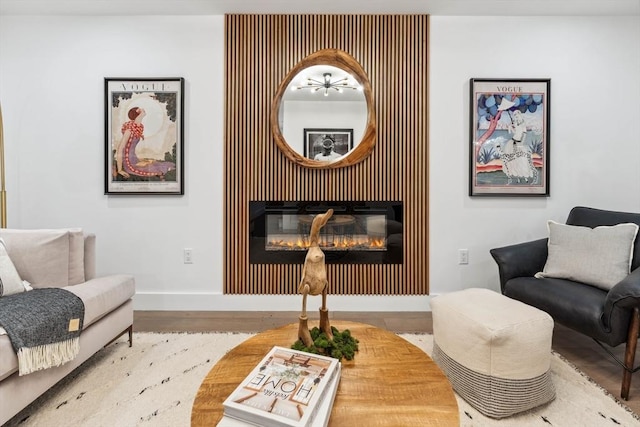 living area with a glass covered fireplace, baseboards, and wood finished floors