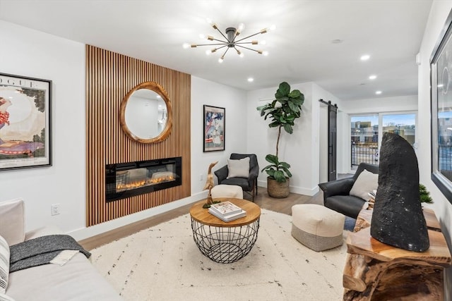 living room with a glass covered fireplace, a barn door, wood finished floors, and baseboards