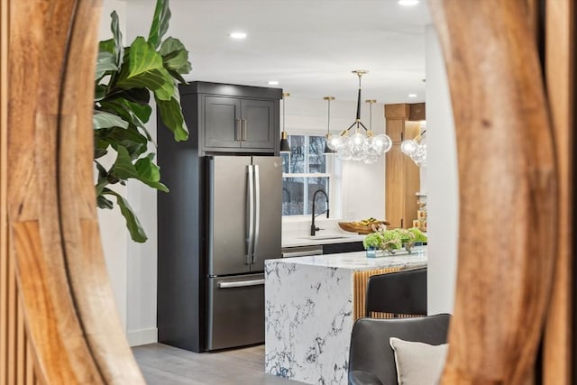 kitchen featuring light stone countertops, light wood-type flooring, a peninsula, freestanding refrigerator, and a sink