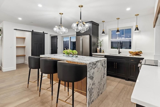 kitchen featuring light wood finished floors, a barn door, appliances with stainless steel finishes, dark cabinetry, and a sink