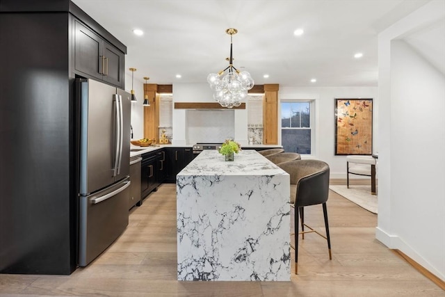 kitchen featuring a kitchen island, a kitchen bar, light wood-type flooring, dark cabinetry, and stainless steel appliances