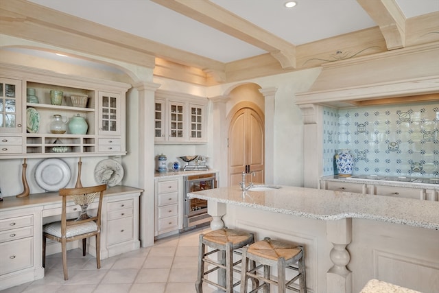 kitchen with a breakfast bar area, light stone countertops, beverage cooler, decorative columns, and sink