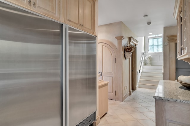 kitchen with stainless steel built in refrigerator, light tile patterned flooring, light brown cabinets, and light stone countertops