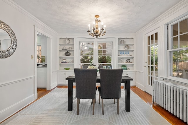 dining room with radiator, built in features, a wealth of natural light, and light hardwood / wood-style flooring