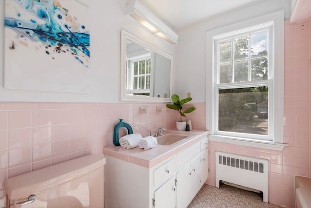 bathroom with a healthy amount of sunlight, radiator, vanity, and tile walls