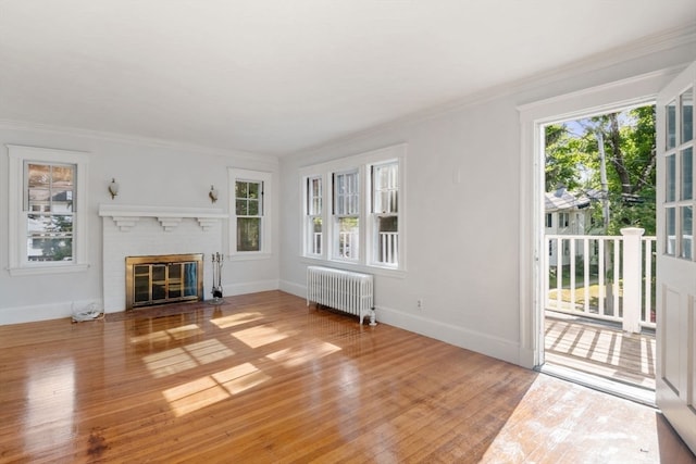 unfurnished living room with ornamental molding, light wood-type flooring, radiator heating unit, and a brick fireplace