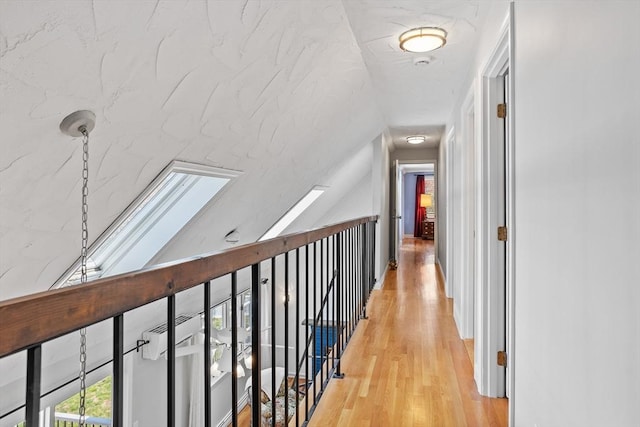 corridor with light wood-type flooring and vaulted ceiling