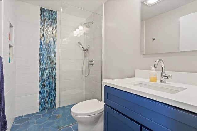full bath with toilet, a tile shower, and vanity