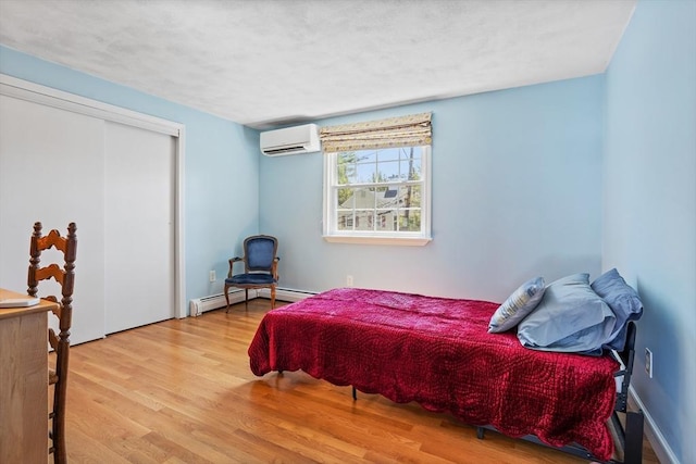 bedroom featuring baseboard heating, a wall mounted AC, a closet, and wood finished floors