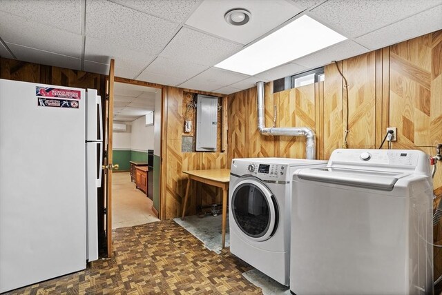 washroom featuring washing machine and clothes dryer, laundry area, wood walls, and electric panel