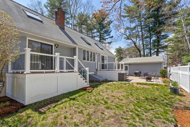 back of property with fence, a deck, a chimney, a patio area, and a lawn