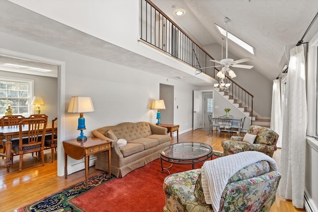 living area featuring wood finished floors, high vaulted ceiling, stairway, a baseboard radiator, and a skylight