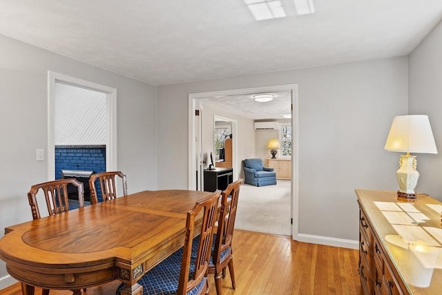 dining area with an AC wall unit, baseboards, a fireplace, and light wood-type flooring