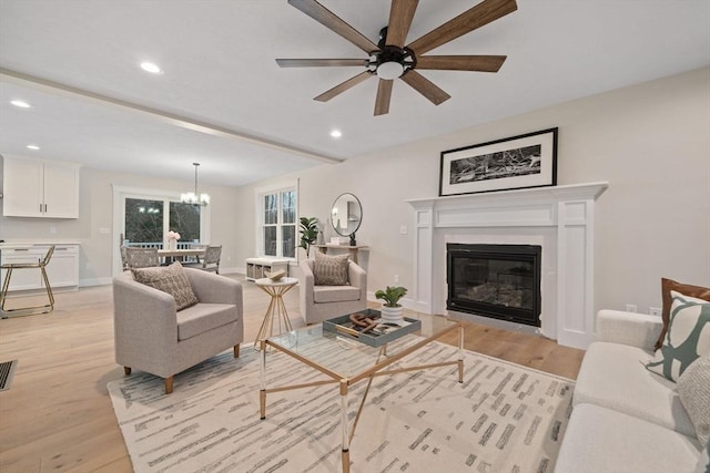 living room featuring ceiling fan with notable chandelier and light wood-type flooring