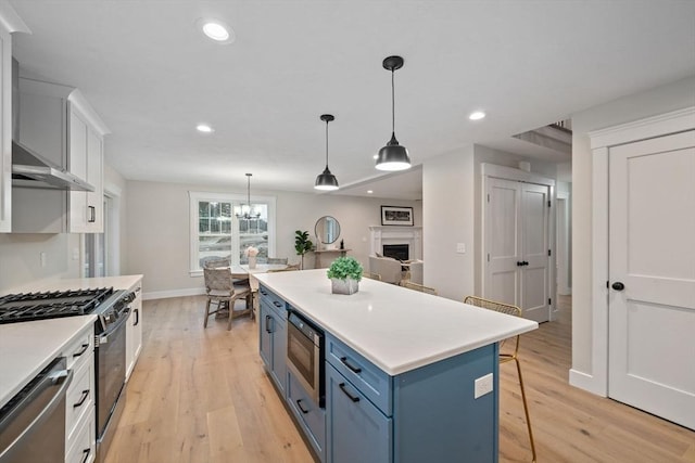 kitchen featuring appliances with stainless steel finishes, a breakfast bar, decorative light fixtures, white cabinets, and blue cabinetry