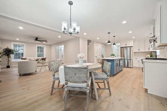 dining area featuring sink, ceiling fan with notable chandelier, and light wood-type flooring