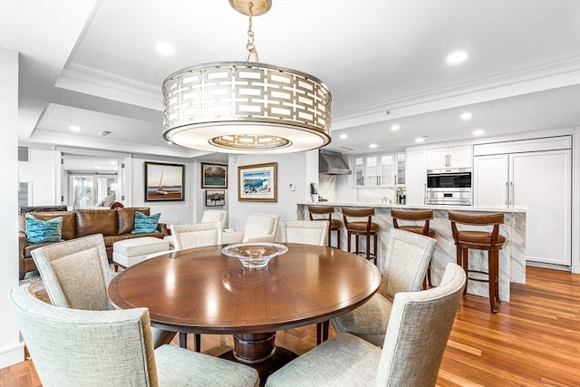 dining area featuring ornamental molding, a tray ceiling, and light wood-type flooring