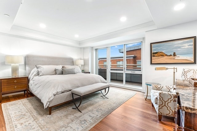 bedroom featuring crown molding, access to outside, light wood-type flooring, and a tray ceiling