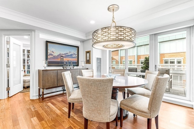 dining space with ornamental molding and light hardwood / wood-style flooring