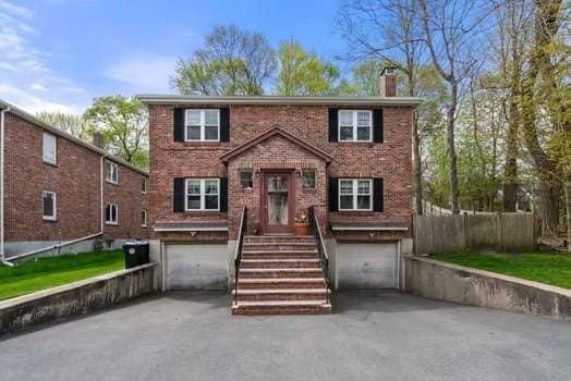 colonial-style house featuring aphalt driveway, brick siding, a chimney, and an attached garage