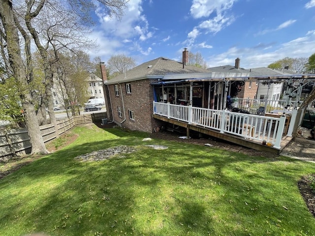 back of house featuring a chimney, brick siding, a fenced backyard, a wooden deck, and a lawn