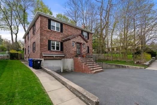view of front of house featuring a garage, a chimney, brick siding, a front lawn, and driveway