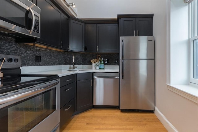 kitchen with appliances with stainless steel finishes, decorative backsplash, light hardwood / wood-style flooring, and sink