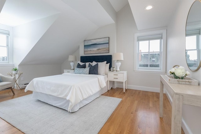 bedroom with multiple windows, a baseboard heating unit, light hardwood / wood-style flooring, and vaulted ceiling