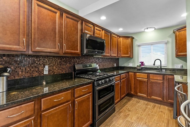 kitchen with recessed lighting, decorative backsplash, appliances with stainless steel finishes, a sink, and dark stone counters