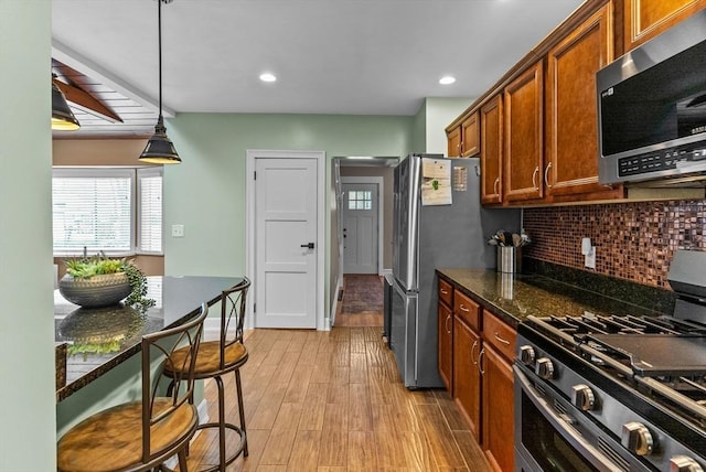 kitchen with tasteful backsplash, brown cabinetry, light wood-style flooring, stainless steel appliances, and pendant lighting