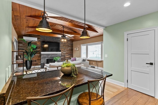 kitchen with baseboards, wood ceiling, decorative light fixtures, a stone fireplace, and light wood-style floors