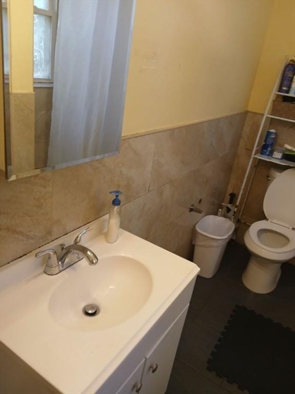 bathroom with toilet, tile walls, vanity, and wainscoting