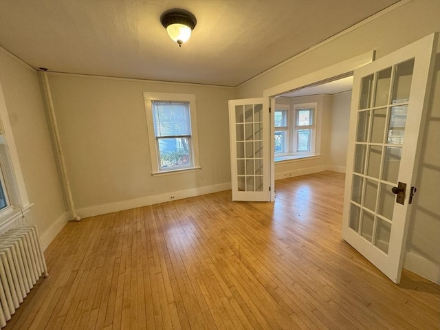 empty room featuring radiator heating unit, light wood-type flooring, french doors, and crown molding