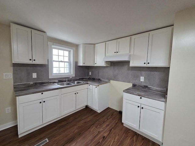 kitchen with dark wood-type flooring, a sink, backsplash, and white cabinets